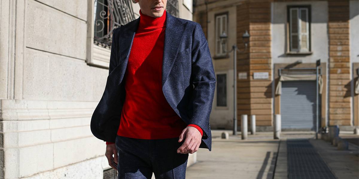 Un uomo indossa un completo blu con maglione dolcevita rosso
