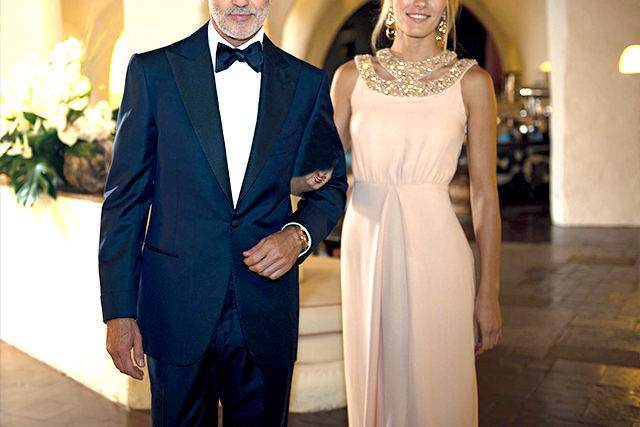 A man wears a blue men's tuxedo with a blue bow tie, accompanied by a woman in a pink dress