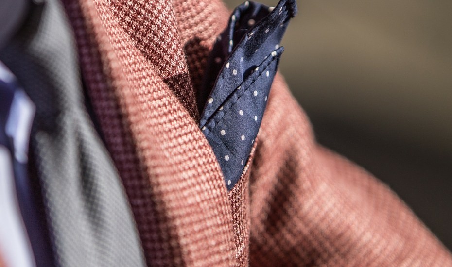 Detail on a blue men's pocket square inserted in the pocket of a brown jacket