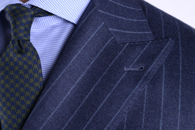Détail sur les revers en pointe d'une veste bleue à rayures, col français d'une chemise à carreaux et cravate verte et bleue