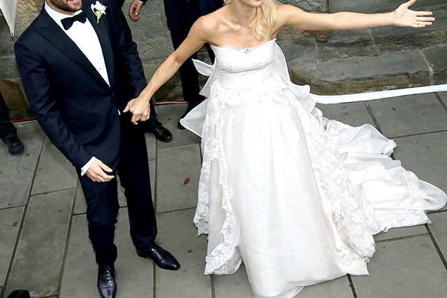 Un uomo indossa uno smoking blu da sposo, accompagnato da una donna in abito da sposa bianco