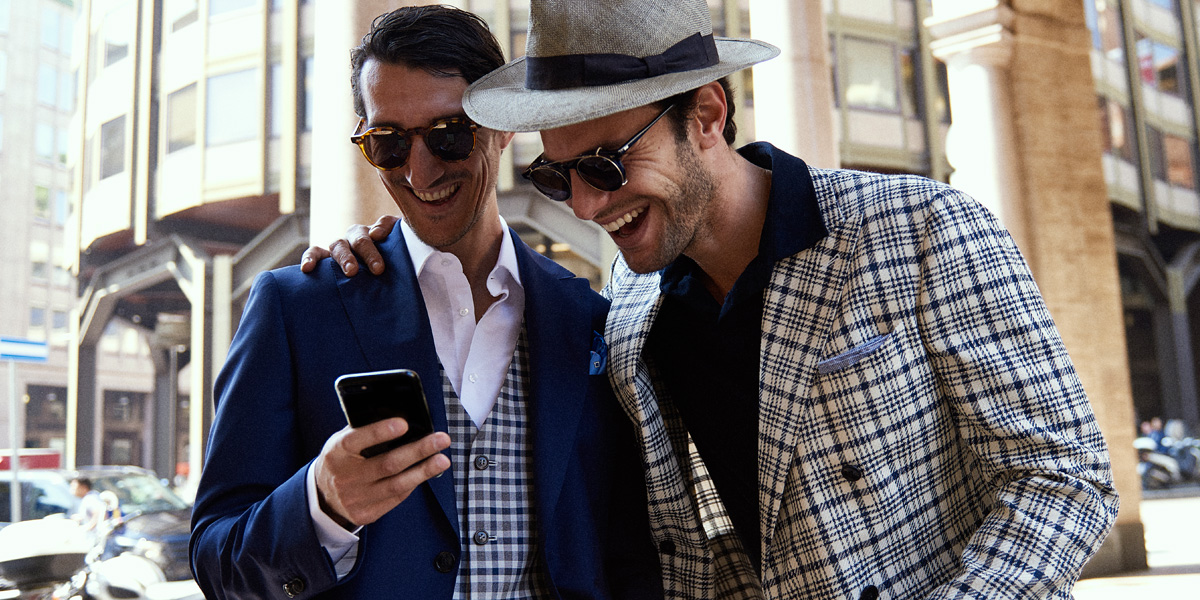 Due uomini indossano completi eleganti e osservano insieme uno smartphone