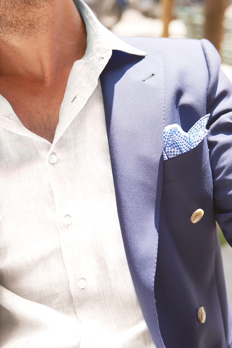 Dettaglio su una camicia bianca in lino, giacca blu con pochette a quadretti blu