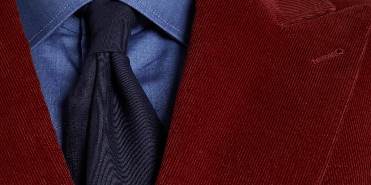 Dettaglio di una giacca in velluto a coste con camicia denim e cravatta blu