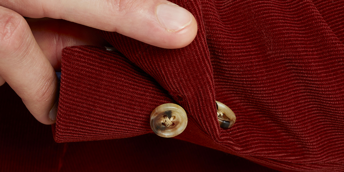 Dettaglio manica con bottone di un blazer in velluto a coste rosso