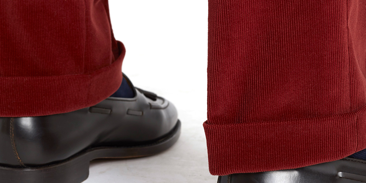 Dettaglio fondo con risvolto di pantaloni in velluto a coste rosso: la lunghezza arriva fino a sfiorare la tomaia della scarpa
