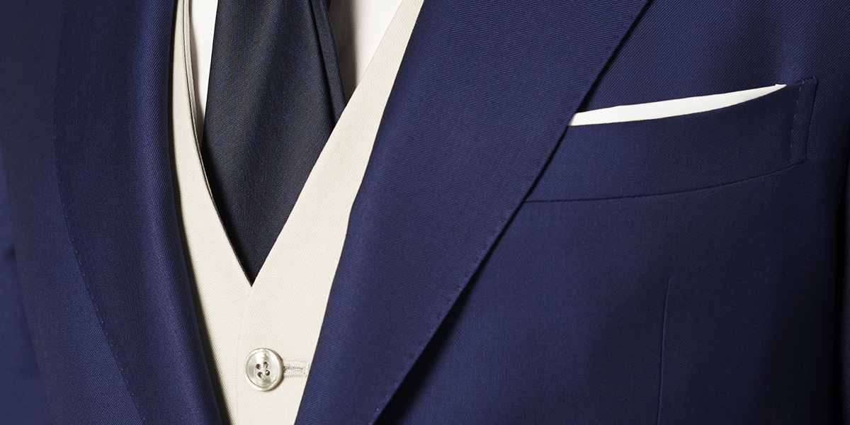 Particolare su un abito blu con gilet panna, cravatta nera, camicia e pochette bianche