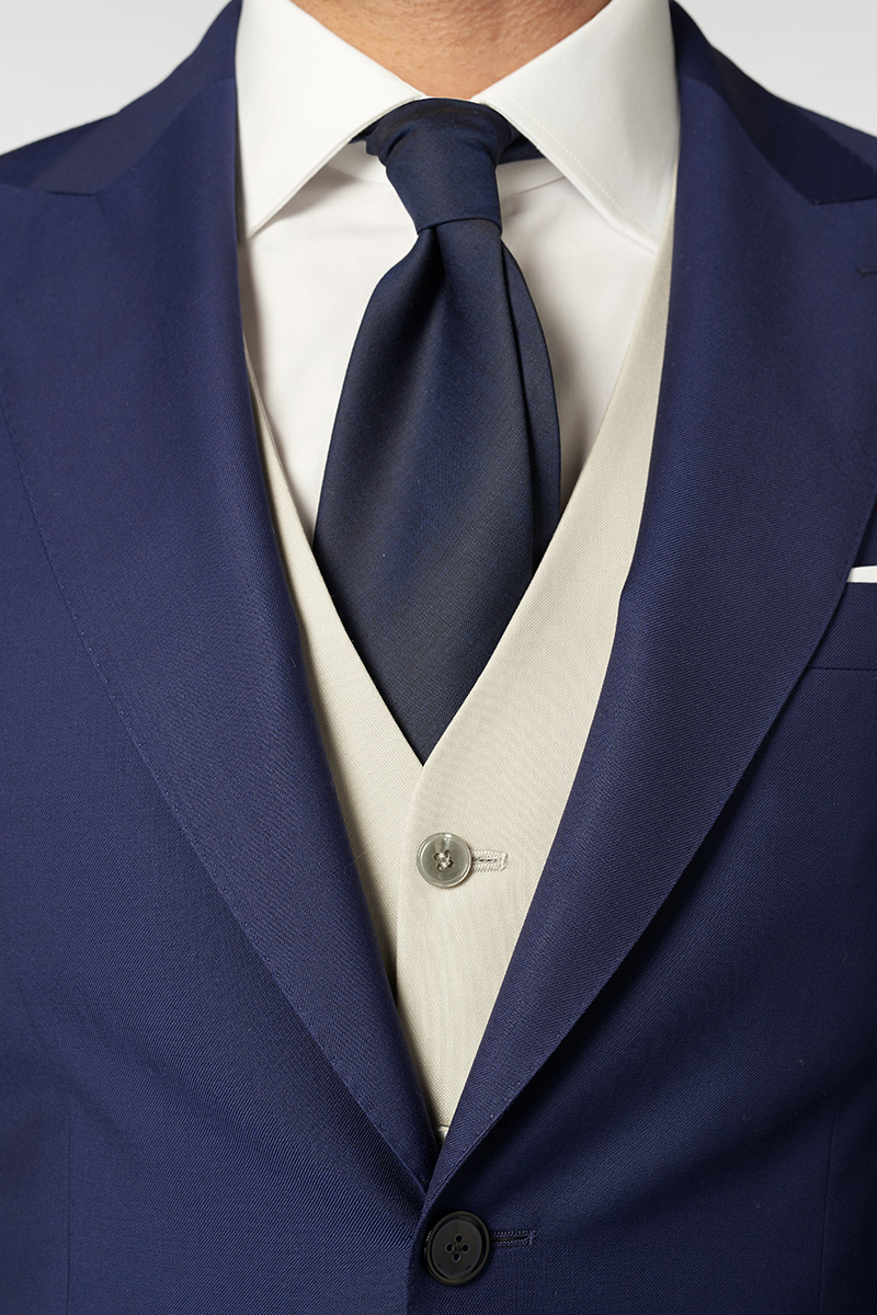 Détails sur le costume bleu, la chemise blanche, le gilet gris clair et la cravate bleue