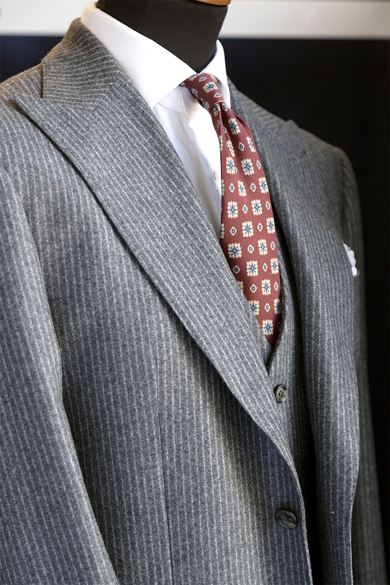 Light gray pinstripe three-piece suit with white shirt and burgundy tie with yellow and blue pattern