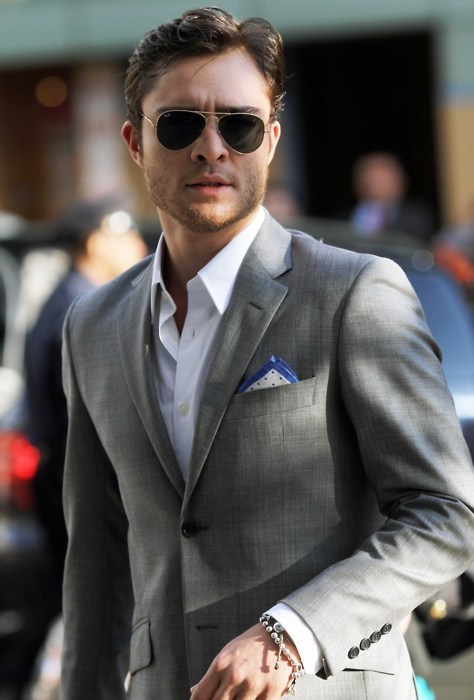 Uomo con occhiali da sole indossa una giacca grigia con pochette piagata a triangolo e camicia bianca