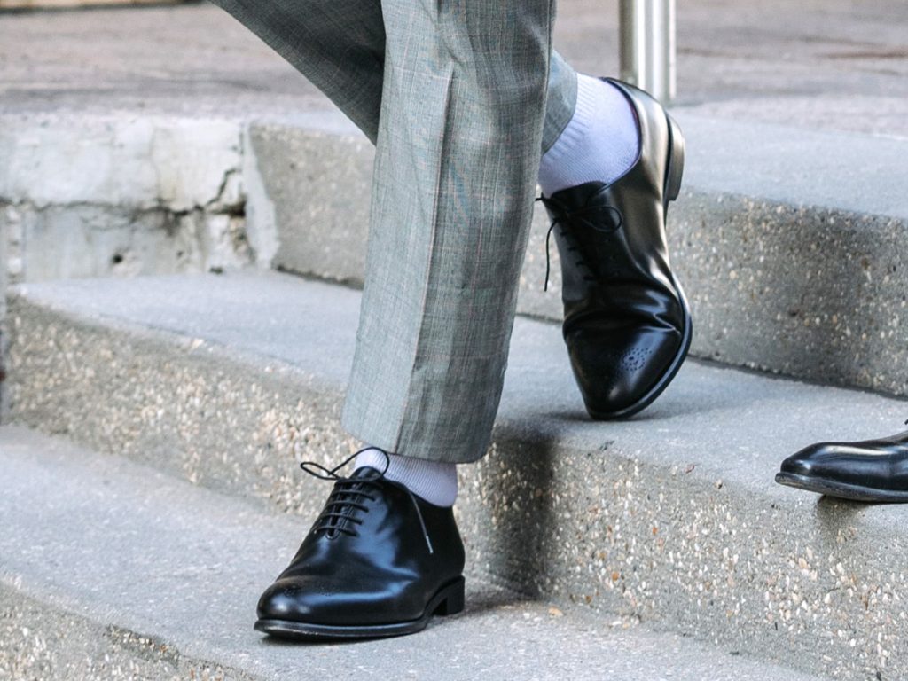 Dettaglio sui calzini bianchi indossati con un paio di scarpe nere eleganti e pantaloni principe di galles 